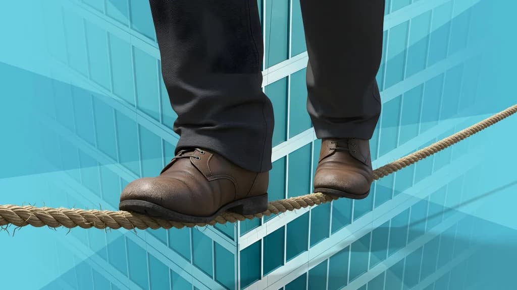 On a blue background with a skyscraper, a man in brown shoes and black slacks walks a tightrope in the foreground. 