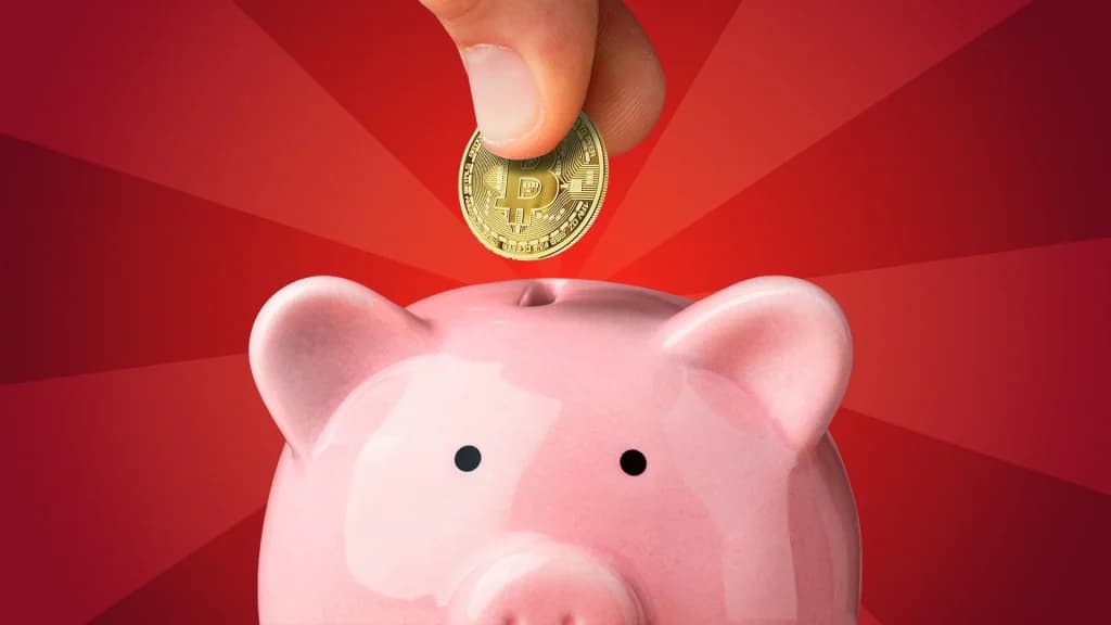 On a red background, a hand drops a Bitcoin into a pink piggy bank.