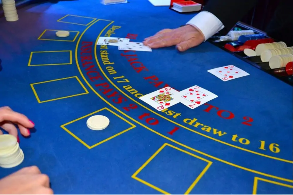 A blue felt poker table with a dealer's right hand over two Blackjack cards