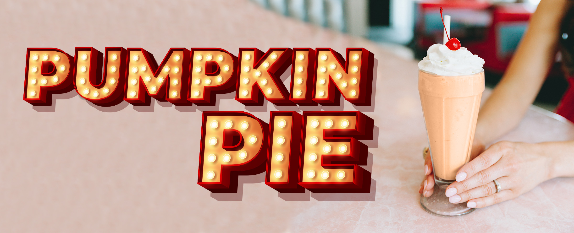 Vegas-style sign saying “pumpkin pie” sits to the left of a milkshake with a cherry on top against the setting of a 50s-style diner