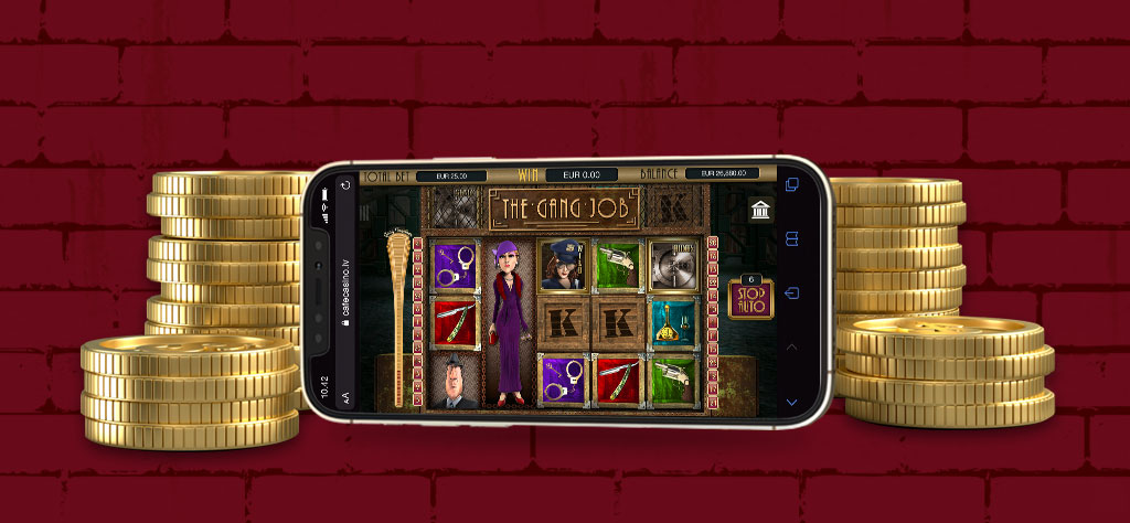The Mob Heist slot from Cafe Casino is display on a mobile phone set in front of a red brick wall with gold coins on either side
