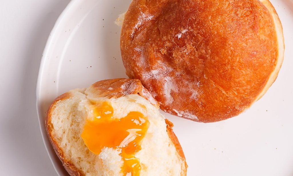 Two donuts sit on a white plate on a white surface