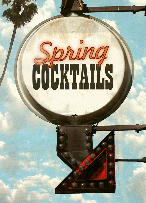 A round, off-white industrial back-lit sign, with Vegas-style arrow hanging beneath it. Inside the sign read the words “Spring Cocktails” in red and black. Behind, is a palm tree set against a blue sky with clouds.