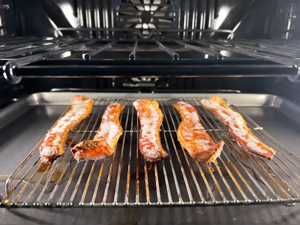 Crispy bacon sits on a small cooking rack on top of a baking sheet inside an oven.