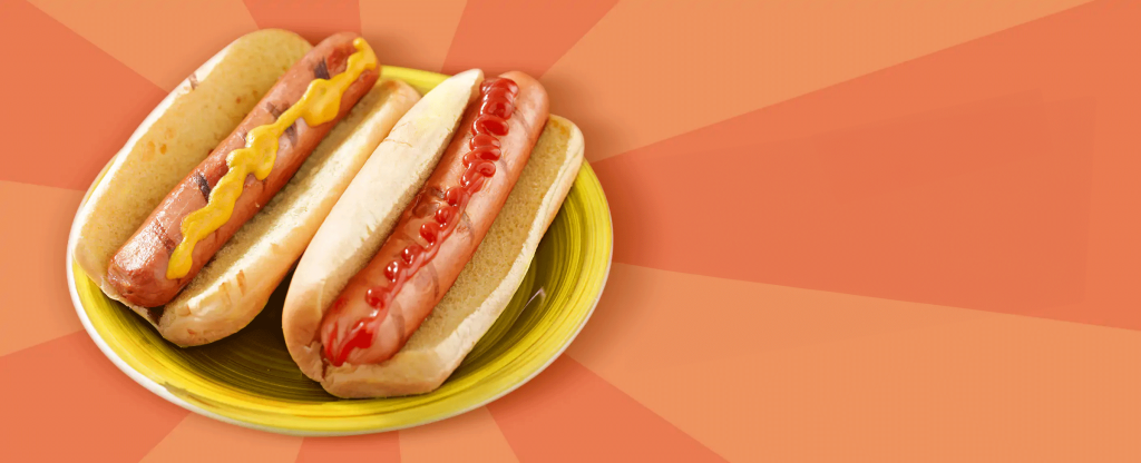 We see two large hotdogs sitting inside buns, one with ketchup and the other with mustard, placed on a yellow plate.