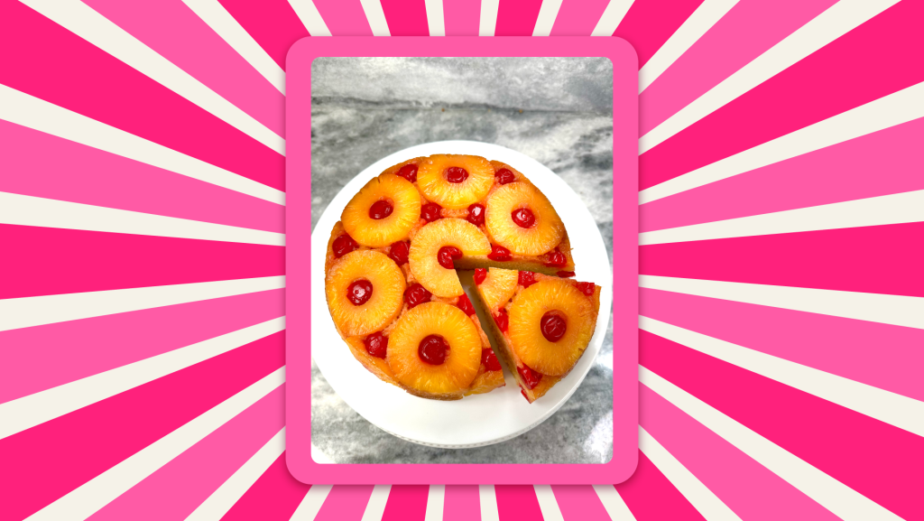 Chef Genevieve’s Pineapple Upside-Down Cake sits on a white cake stand on a marble countertop with a slice cut out, but not removed.