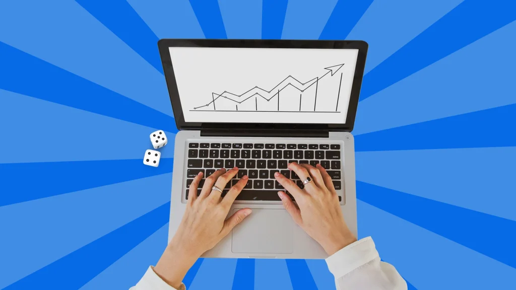A laptop with an upward trending graph on screen shows on a blue background with 2 dice next to it